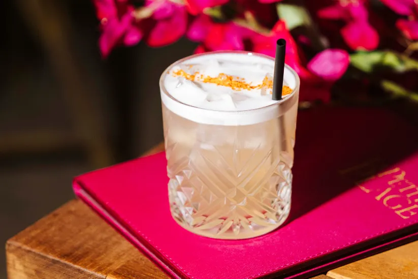 Verre taillé contenant une boisson claire avec glace, mousse et paille noire sur un livre rouge.