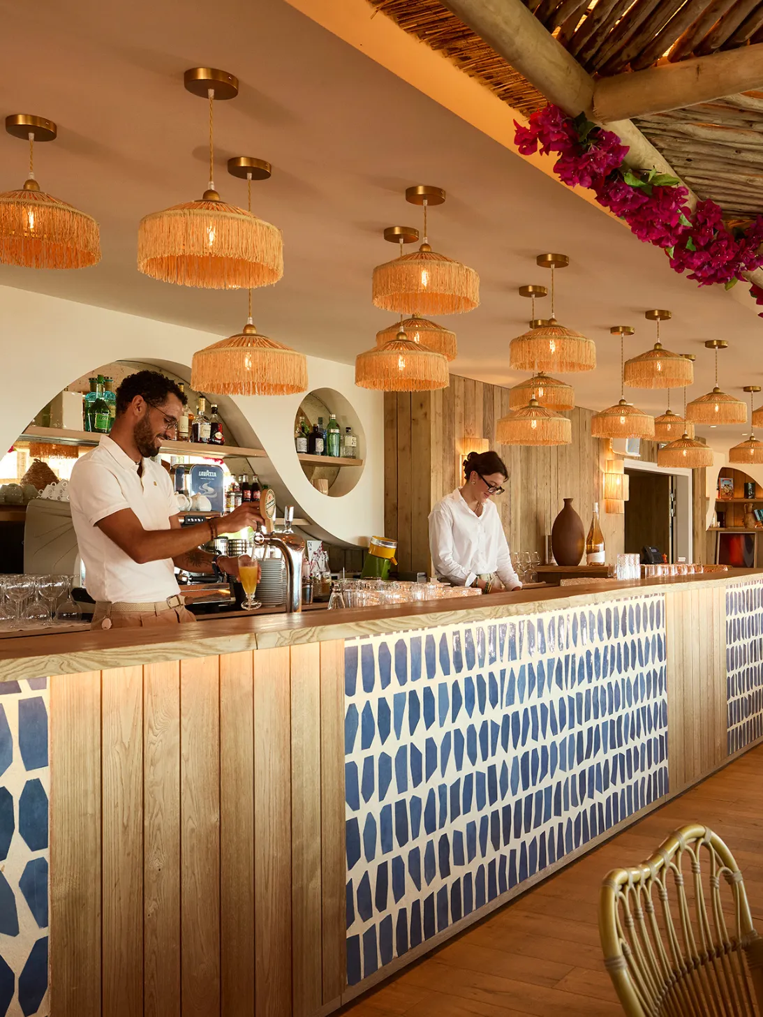 Deux barmans dans un bar au design naturel avec un comptoir en bois et motifs bleus.