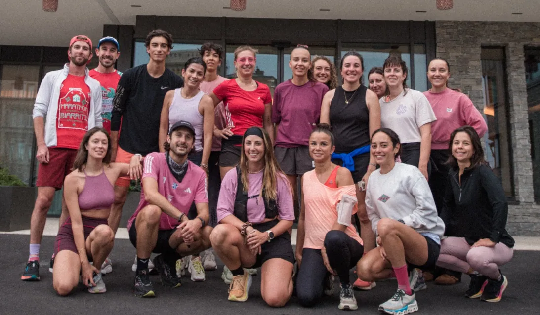 Groupe de 17 coureurs posant devant un bâtiment, en tenue sportive colorée, souriants.