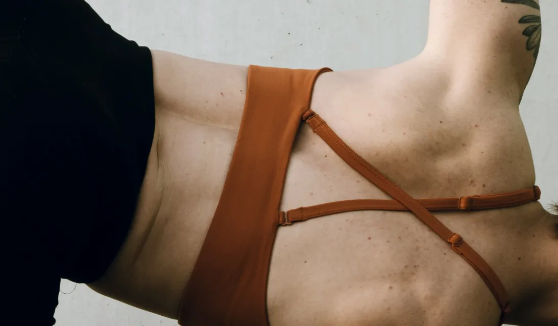 Dos nu d'une personne portant un haut de sport à bretelles croisées orange et des leggings noirs.