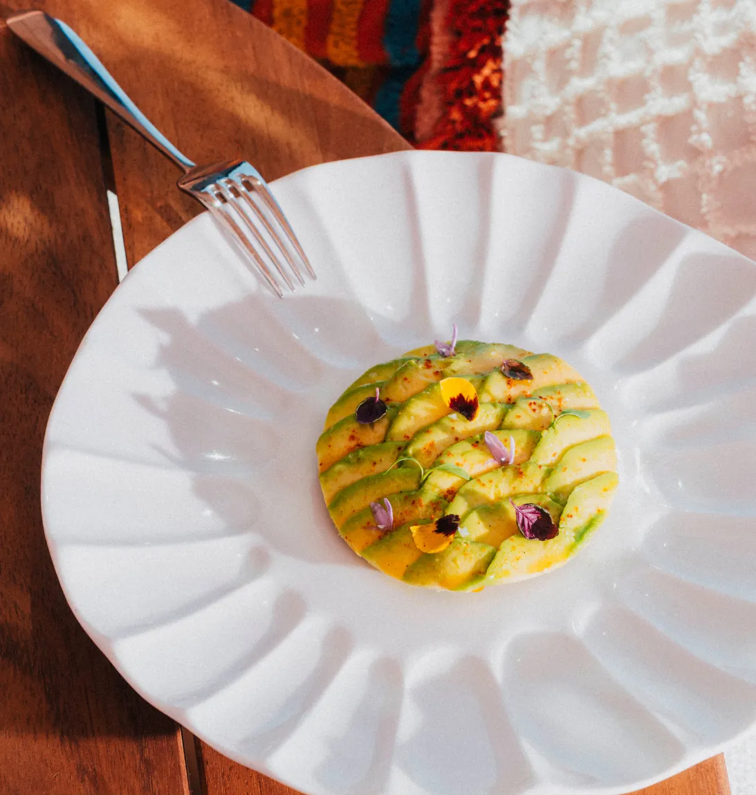White plate with sliced avocado decoration and edible flowers in the center.
