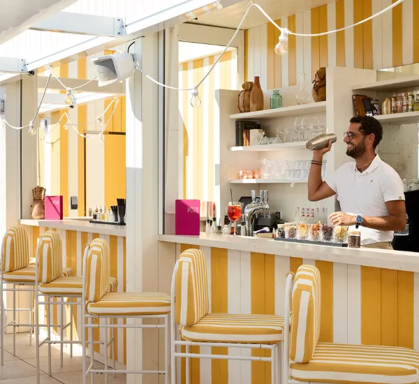 Barman dans un bar à rayures jaunes et blanches préparant un cocktail avec un shaker.