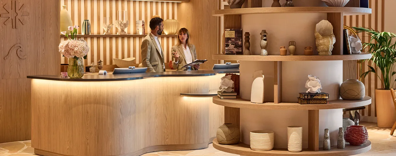 Deux personnes discutent derrière un comptoir en bois avec des étagères décorées d'objets d'art.