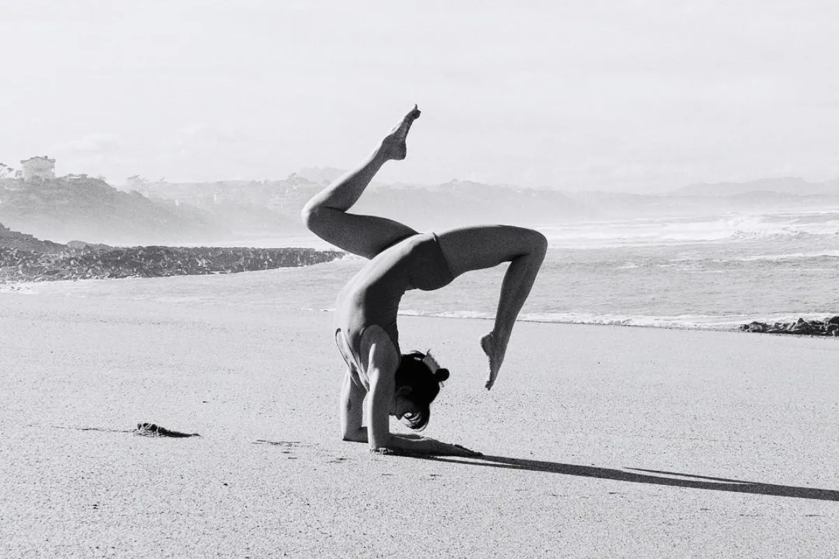Une femme fait une posture de yoga équilibrée sur les avant-bras sur la plage au bord de la mer.