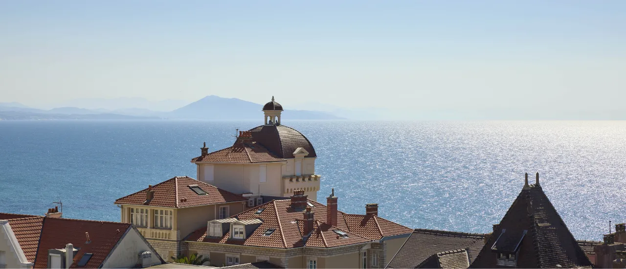 View over roofs with red tiles facing the sparkling sea and distant mountains.