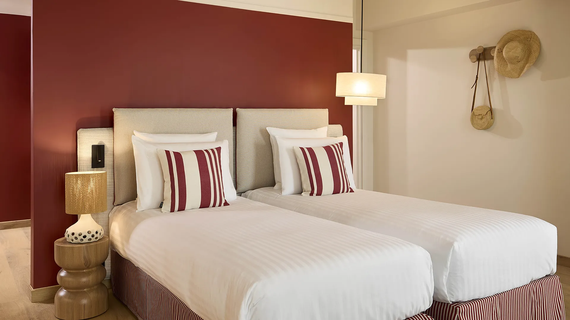 Chambre twin d'hôtel avec deux lits, coussins rayés bordeaux et mur d'accent rouge