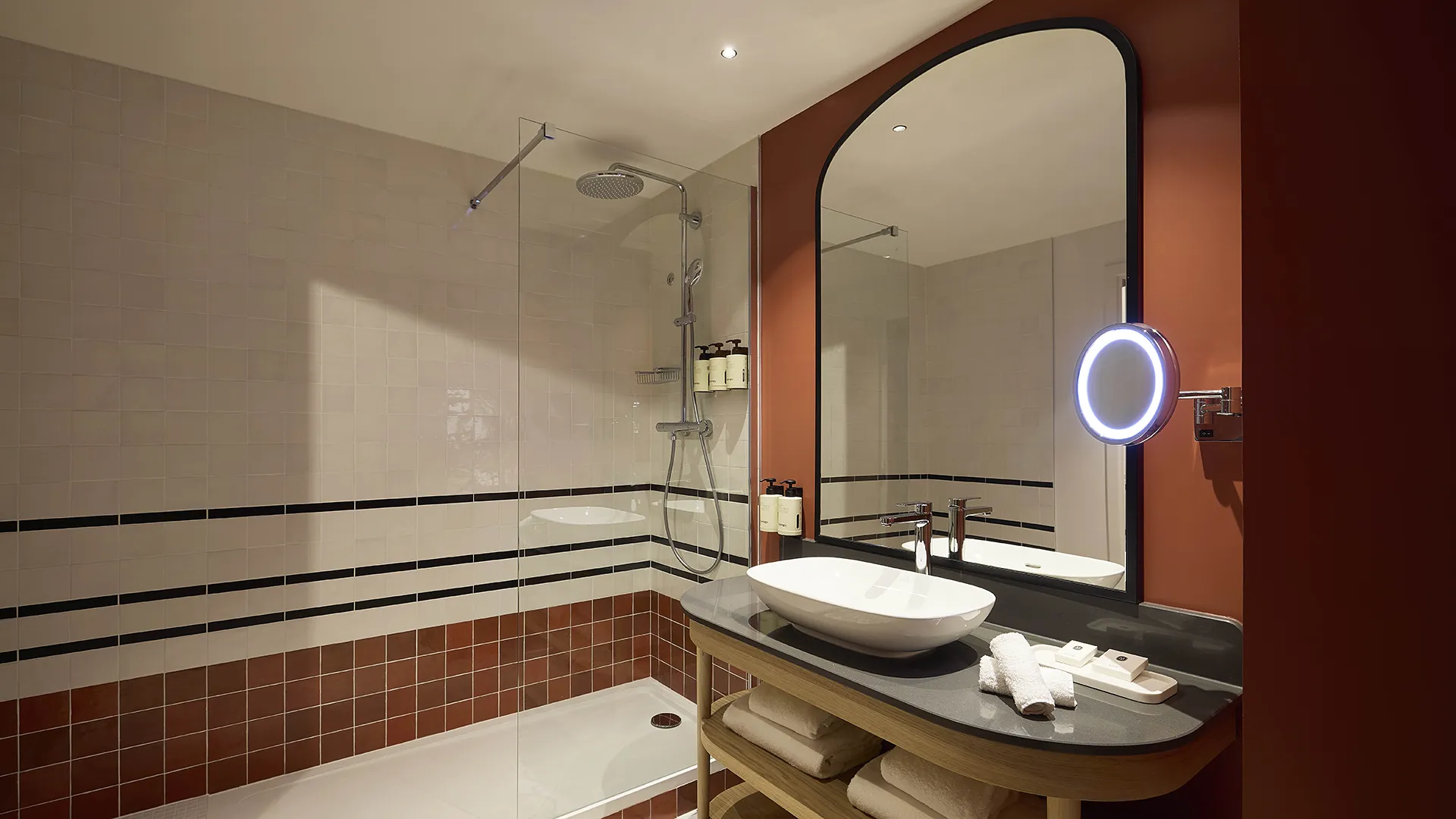 Salle de bain d'hôtel avec double vasque, grand miroir et carrelage terracotta aux accents noirs
