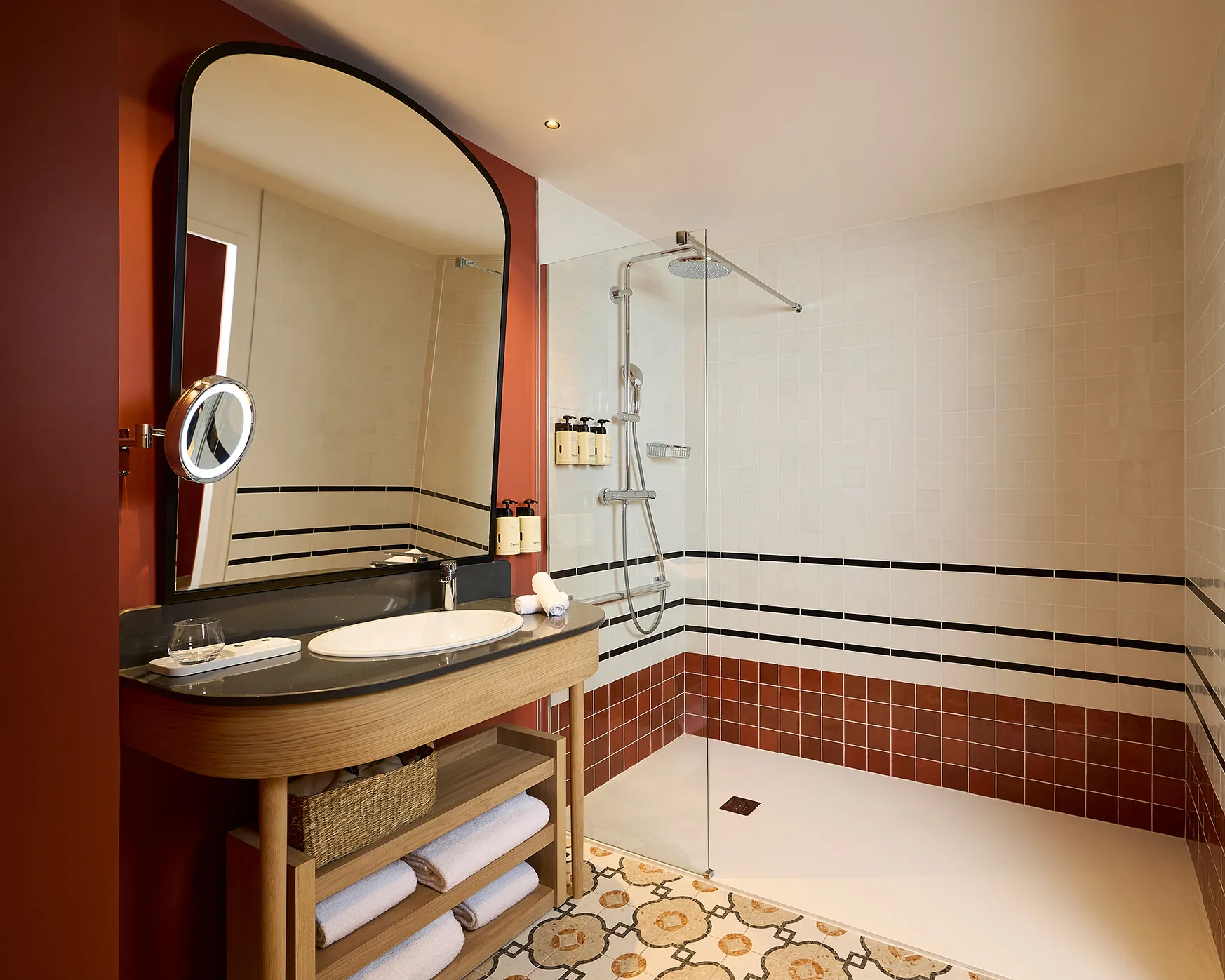 Salle de bain d'hôtel avec vasque, miroir arrondi et baignoire carrelée terracotta