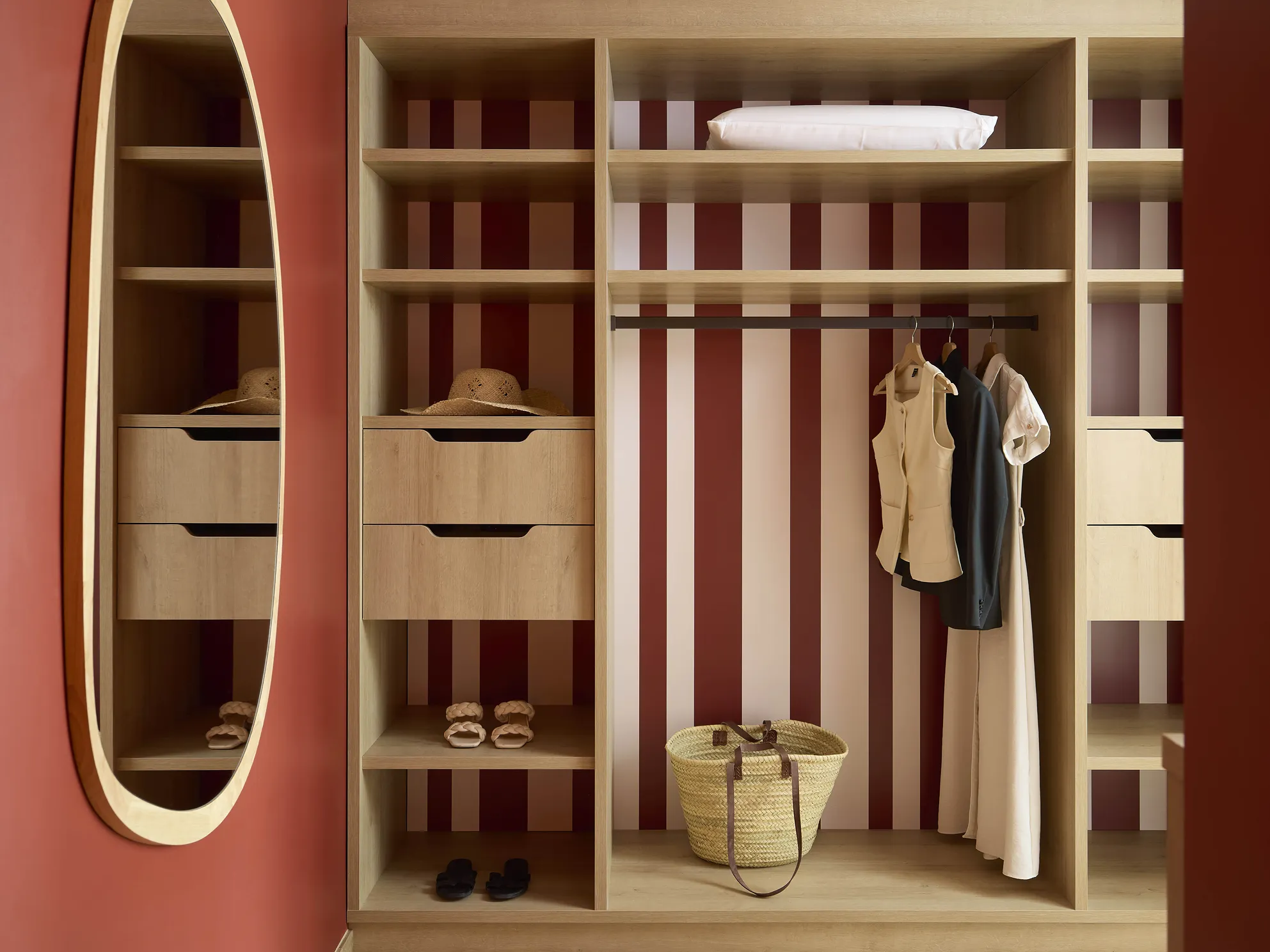 Dressing ouvert en bois clair avec fond rayé bordeaux, miroir ovale et penderie dans une chambre de l'hôtel Le Talaia Mgallery Biarritz