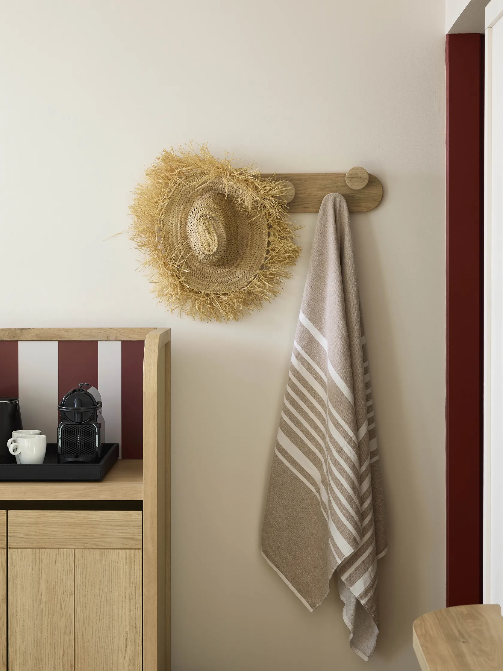 Coin entrée de chambre d'hôtel avec serviette, chapeau de paille et meuble en bois clair