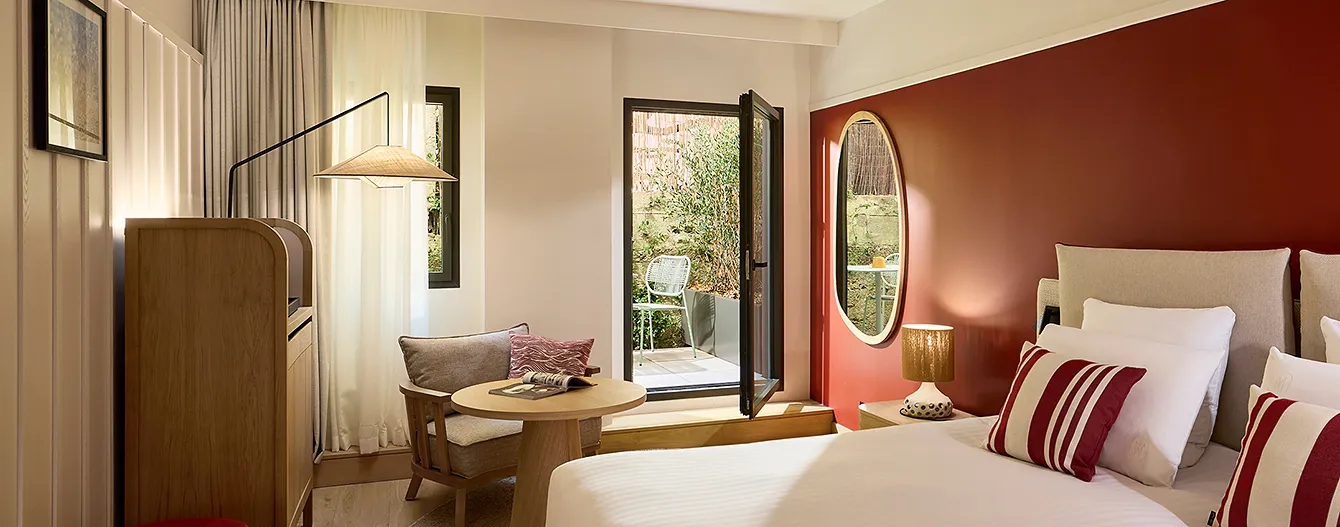 Hotel room with a double bed, a terracotta feature wall, an oval mirror and direct access to a green terrace