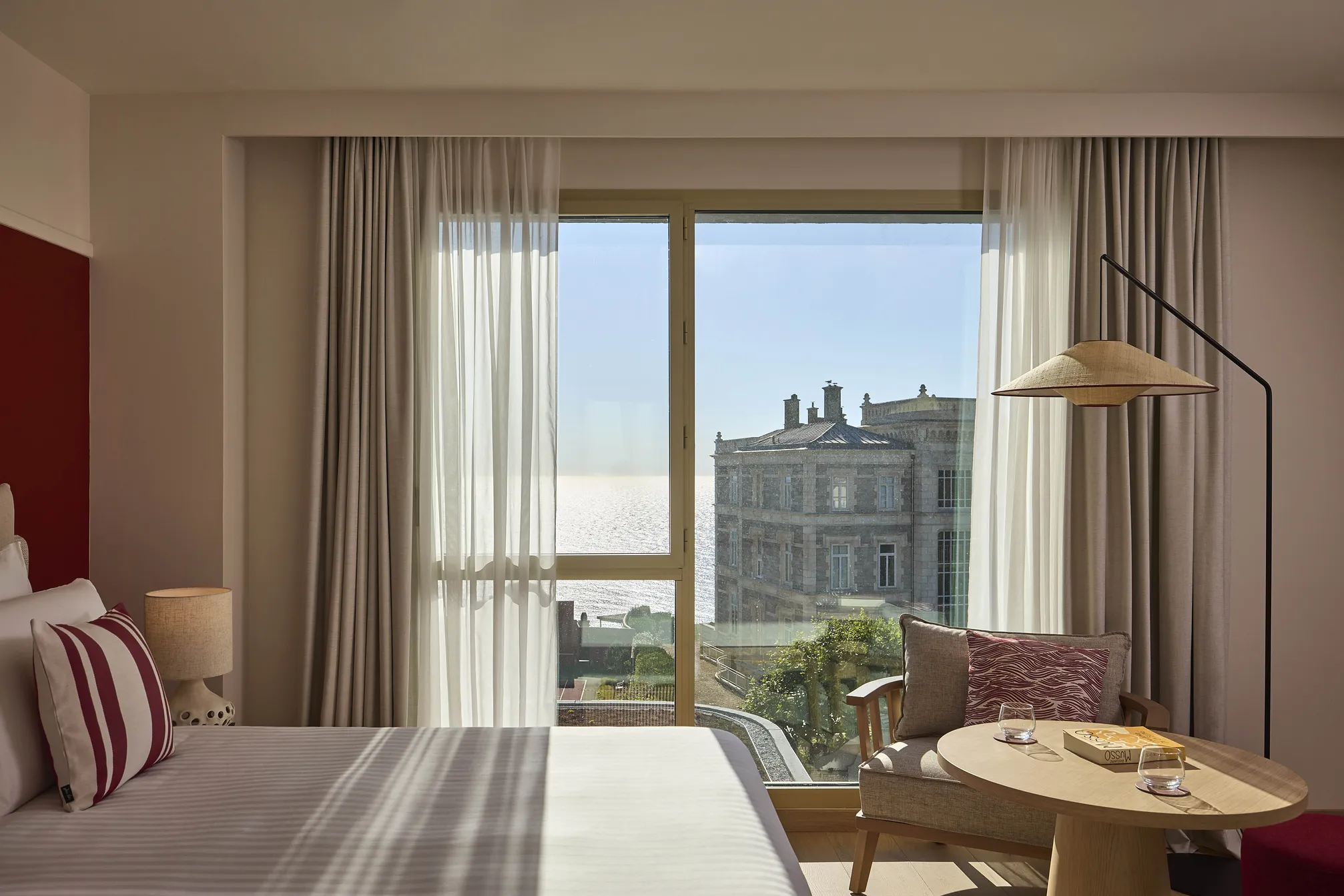 Chambre d'hôtel moderne avec lit, bureau et vue sur la mer à travers de grandes fenêtres lumineuses