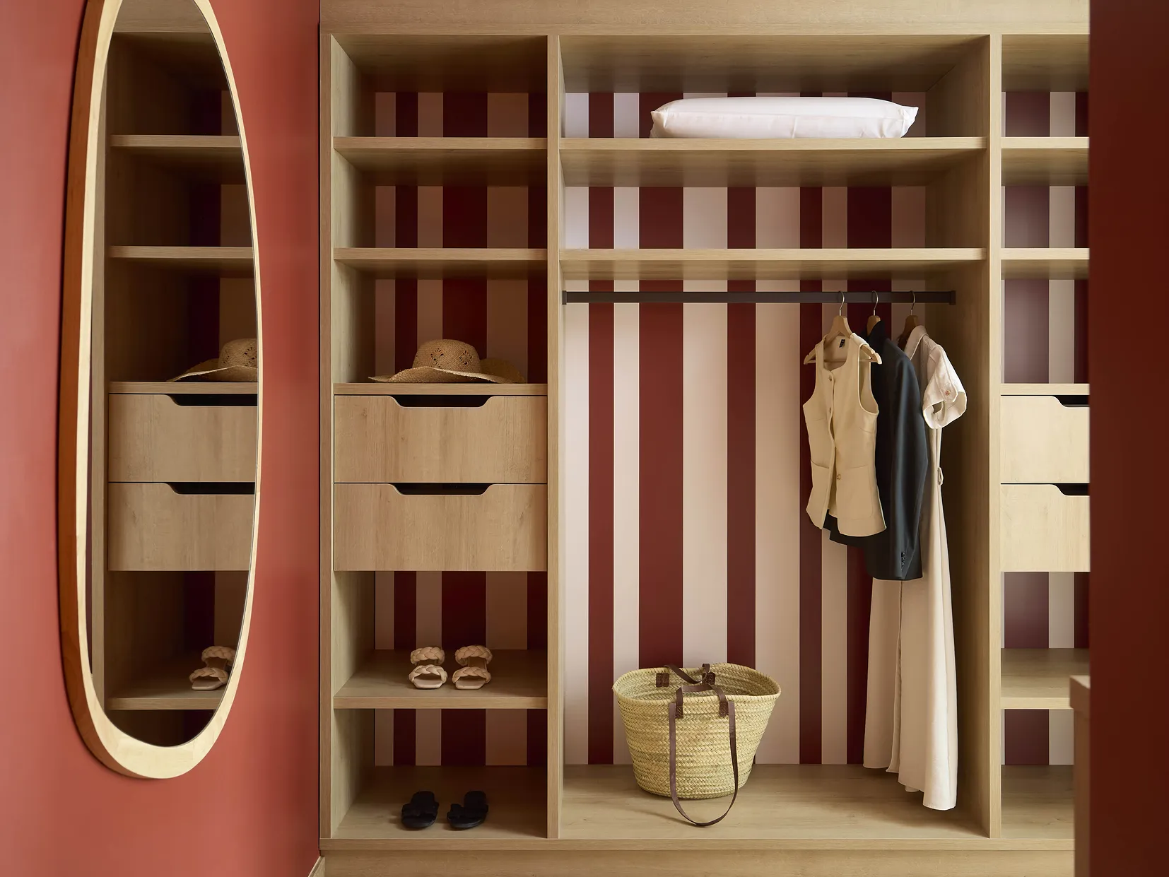 Dressing ouvert avec rangements en bois et miroir ovale aux accents bordeaux dans une chambre de l'hôtel Le Talaia Mgallery Biarritz
