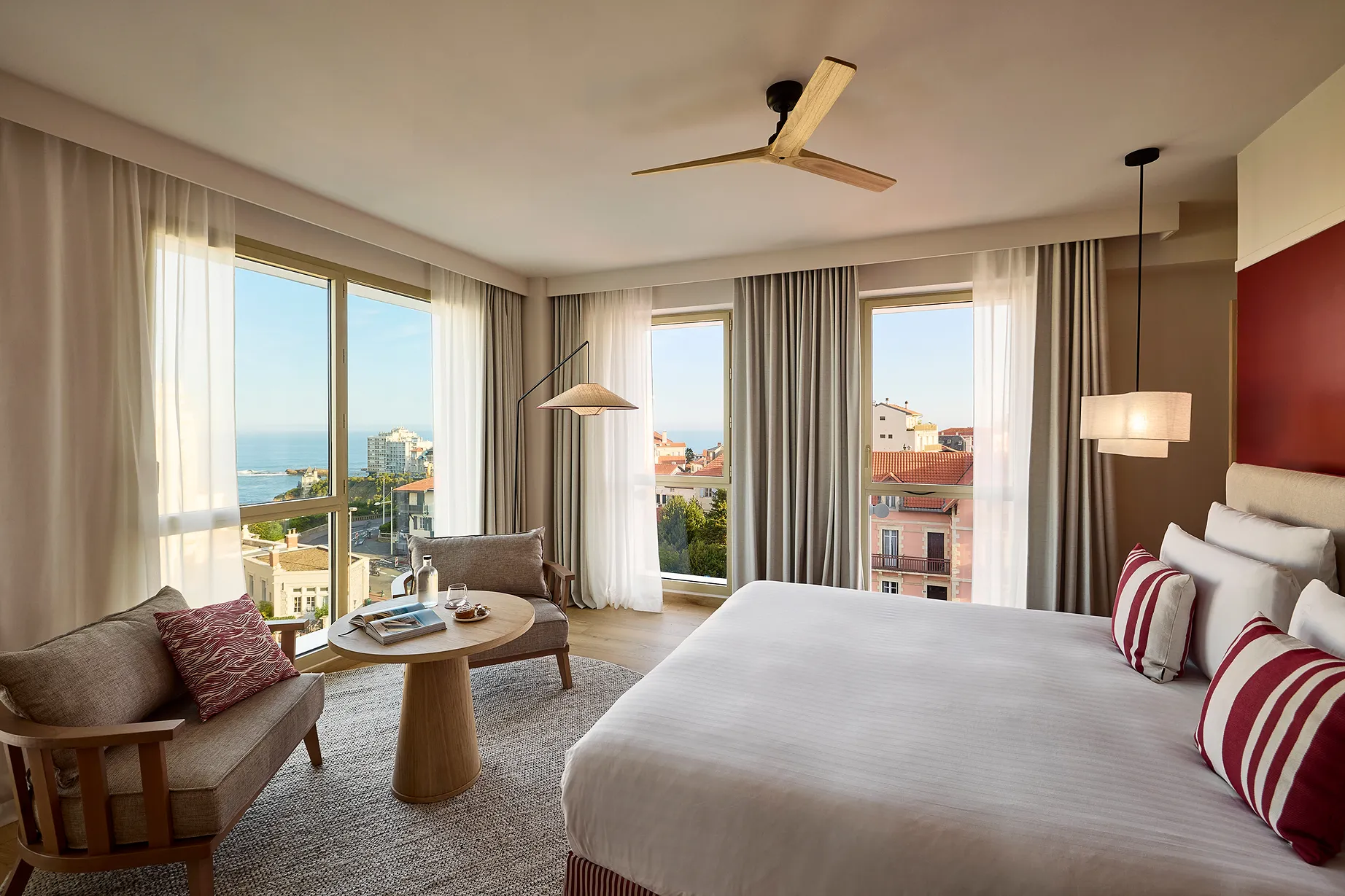 Chambre d'hôtel spacieuse avec grand lit blanc, décor chaleureux en tons rosés et vue sur la ville