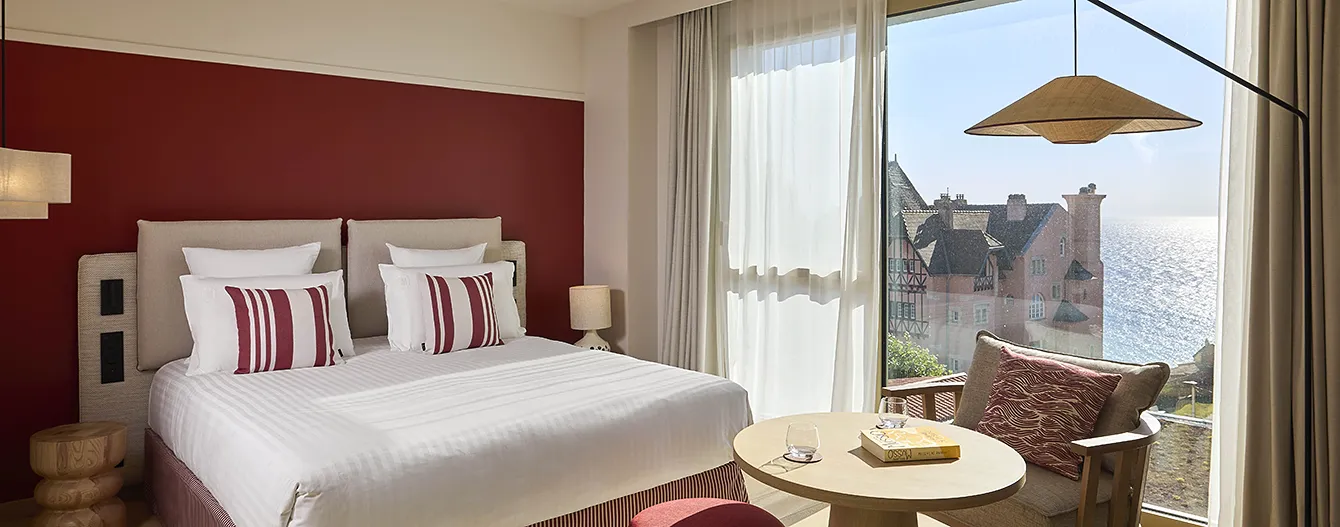 Double room at the Le Talaia Mgallery hotel in Biarritz, featuring a king-size bed, burgundy walls and views of Villa Belza and the ocean