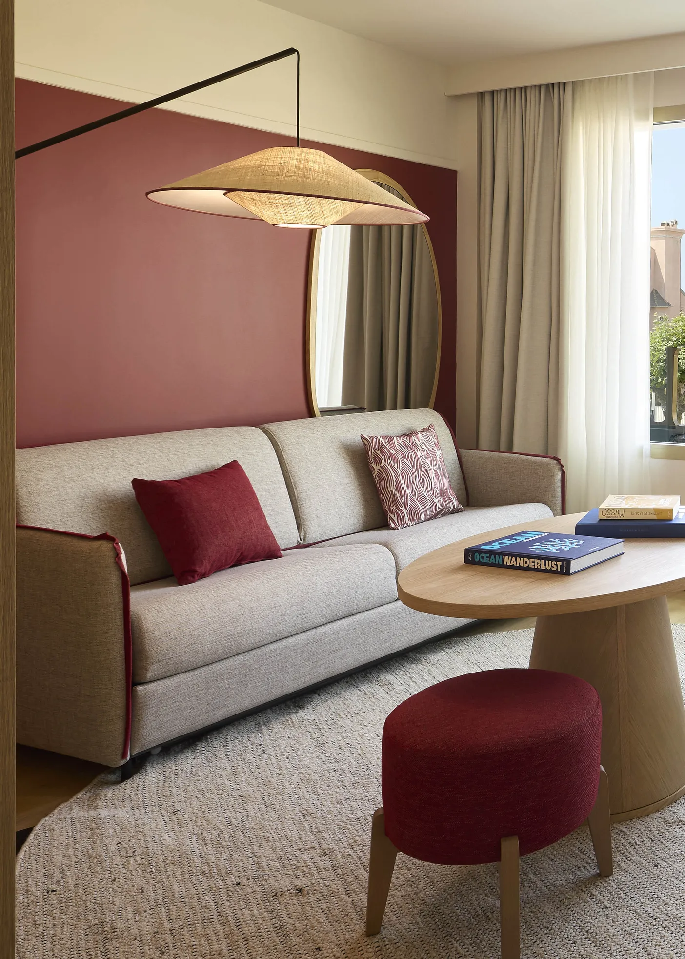 Coin salon d'une chambre de l'hôtel Le Talaia Mgallery Biarritz avec canapé beige, table ronde en bois et pouf bordeaux