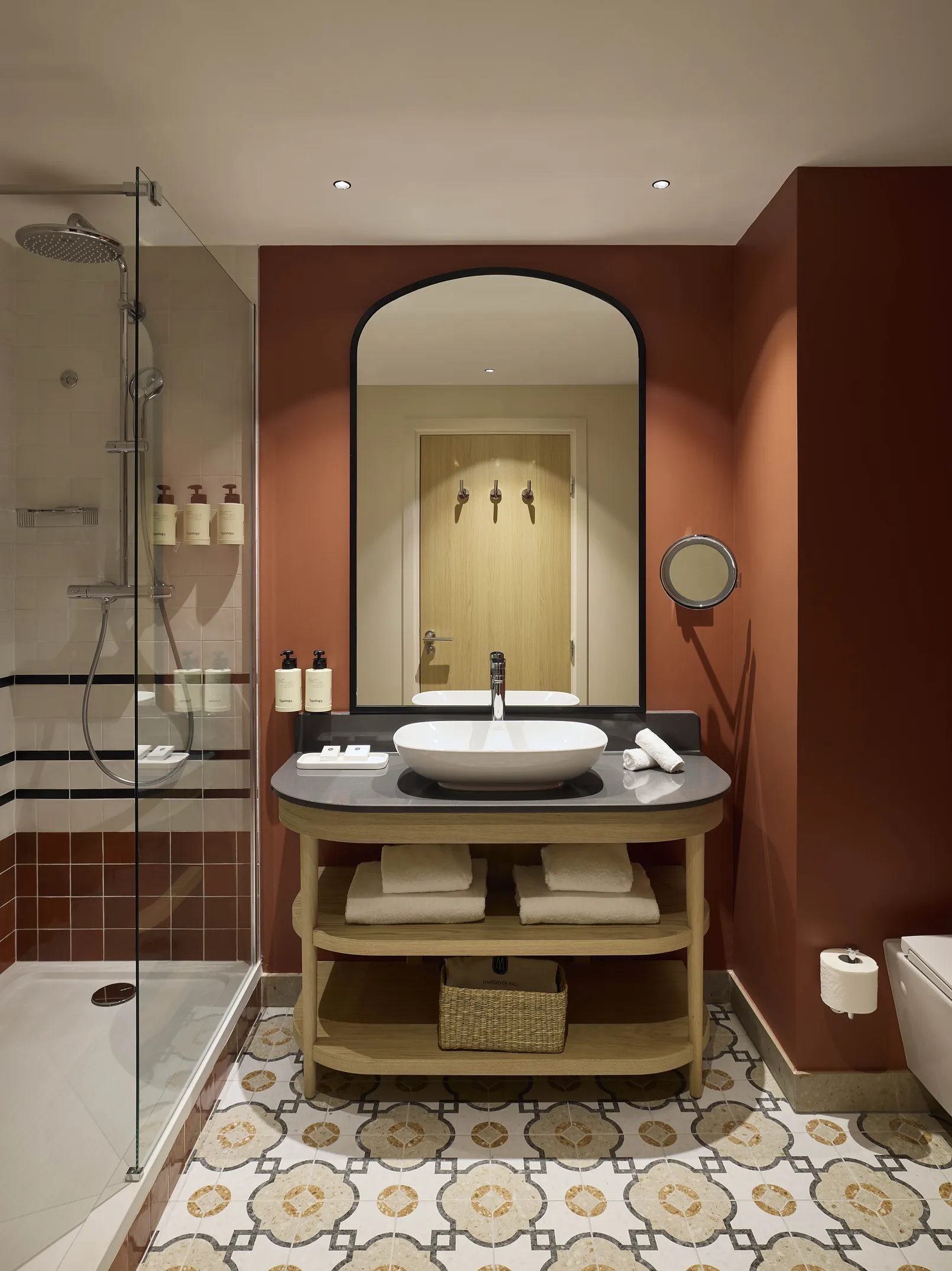 Salle de bain de l'hôtel Le Talaia Mgallery Biarritz avec double vasque, miroir cintré, murs terracotta et carrelage au sol