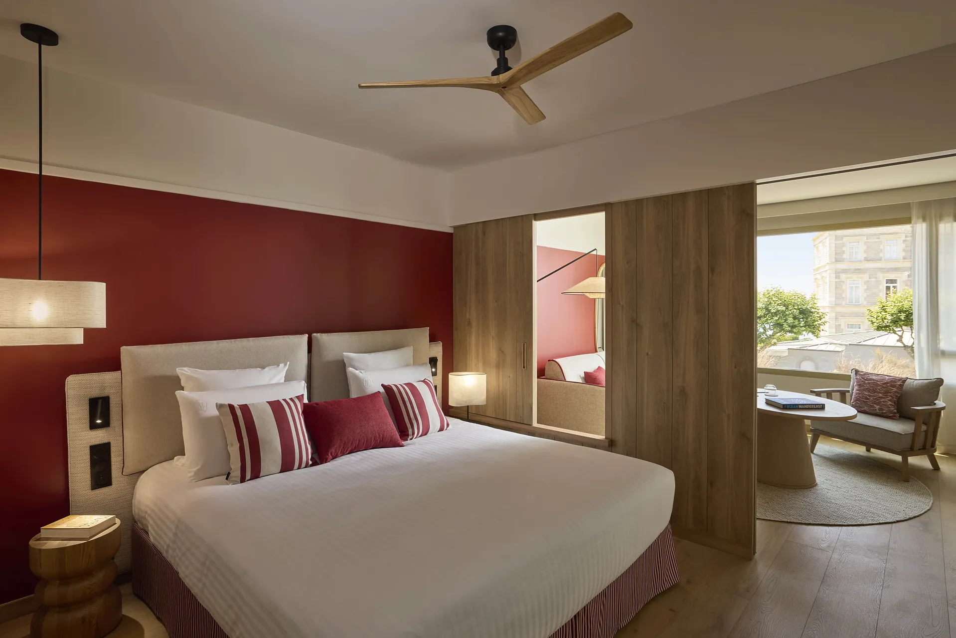 Chambre de l'hôtel Le Talaia Mgallery Biarritz avec lit king-size, mur bordeaux, ventilateur de plafond et accès au salon