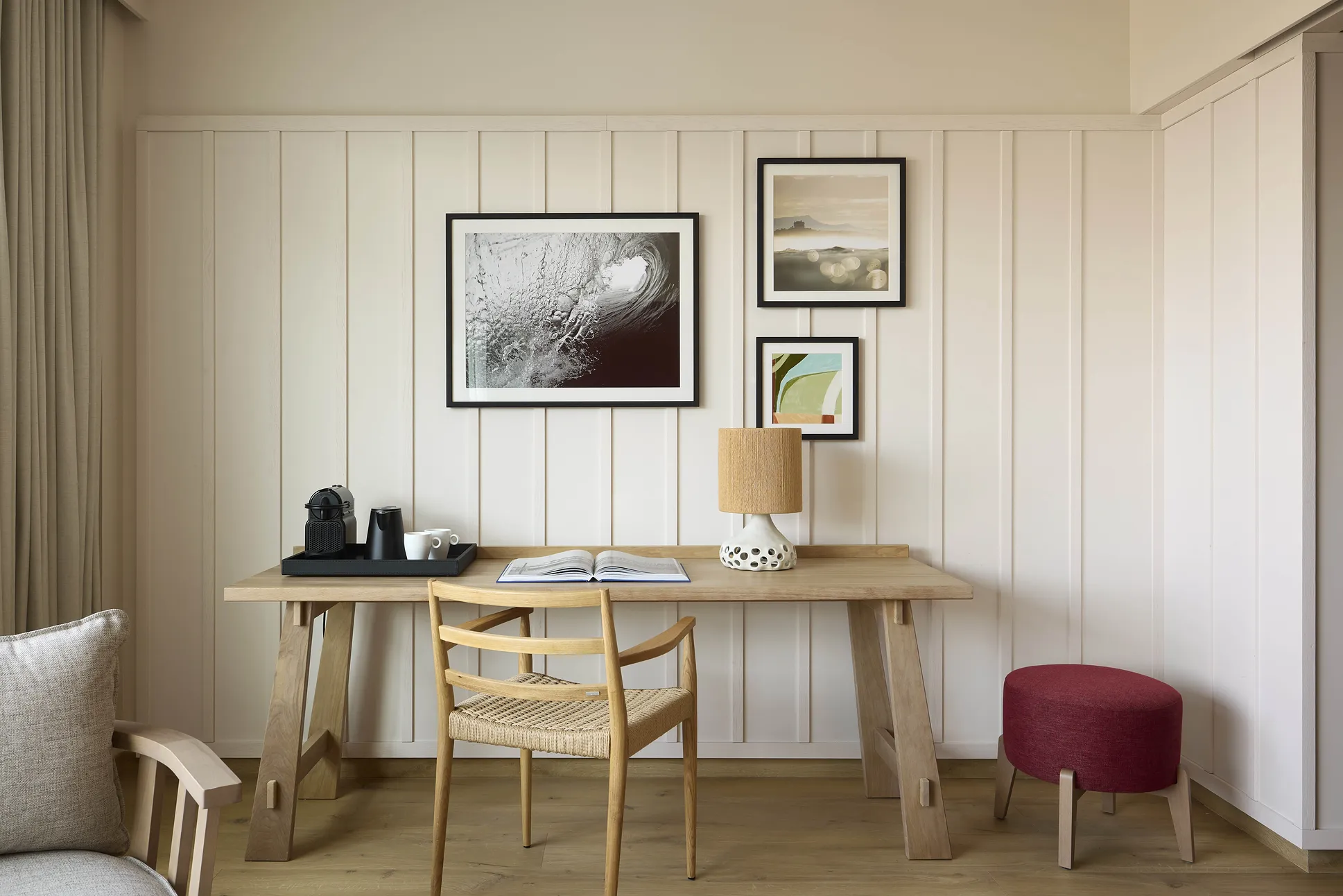 Coin bureau en bois clair avec chaise cannée, tabouret bordeaux et cadres photos au mur dans une chambre de l'hôtel Le Talaia Mgallery Biarritz