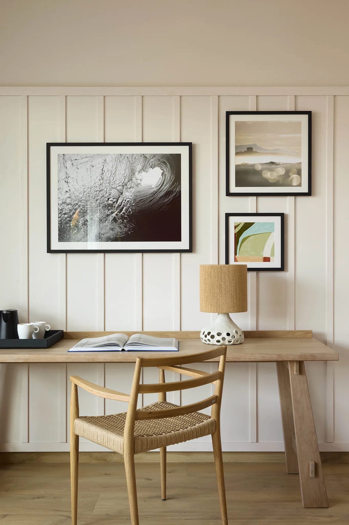 Bureau en bois clair avec chaise cannée et galerie de cadres photos au mur dans une chambre de l'hôtel Le Talaia Mgallery Biarritz