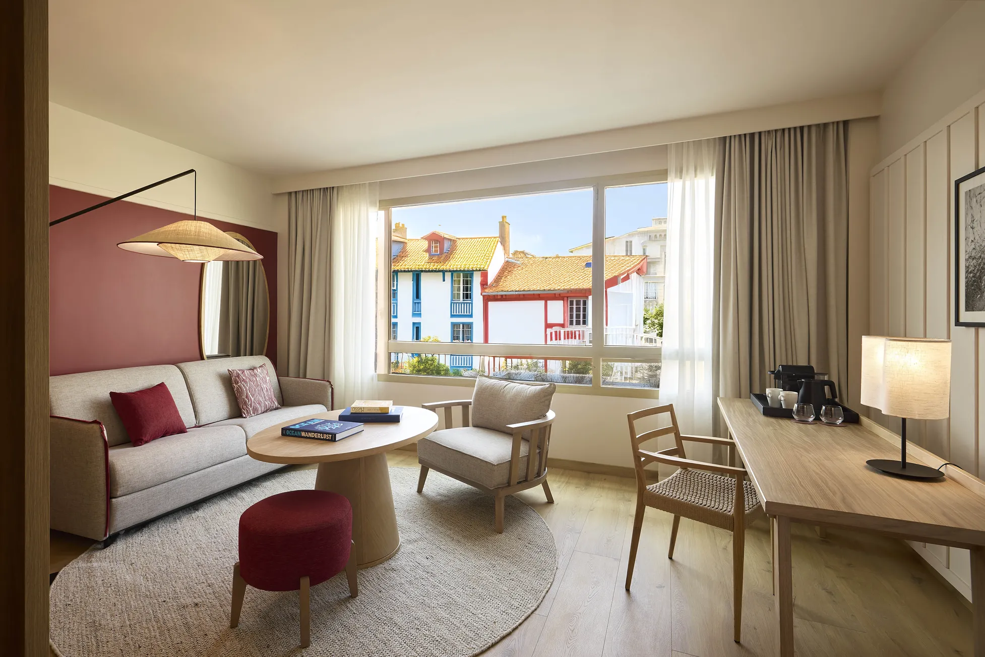 Salon d'une suite de l'hôtel Le Talaia Mgallery Biarritz avec canapé beige, accents bordeaux et vue sur la ville