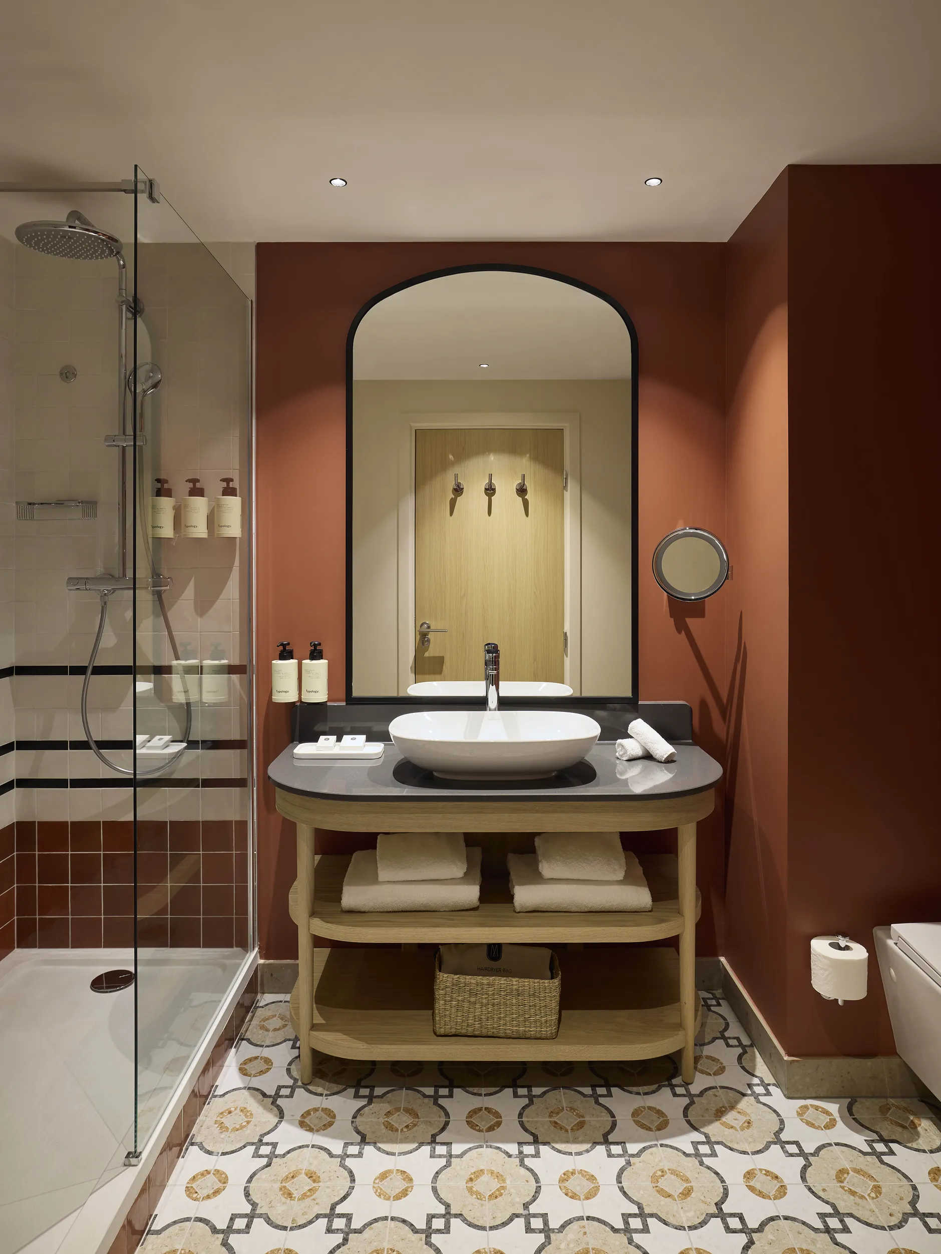 Salle de bain de l'hôtel Le Talaia Mgallery Biarritz avec vasque ronde, miroir cintré, murs terracotta et douche à l'italienne