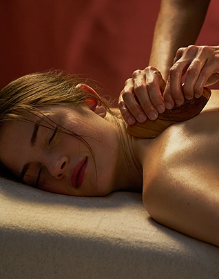 Femme allongée sur une table de massage recevant un massage du dos aux mains chaudes, dans une ambiance lumineuse et chaleureuse aux tons ocre et terracotta