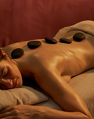 Femme allongée recevant un massage aux pierres chaudes sur le dos dans une ambiance tamisée au spa