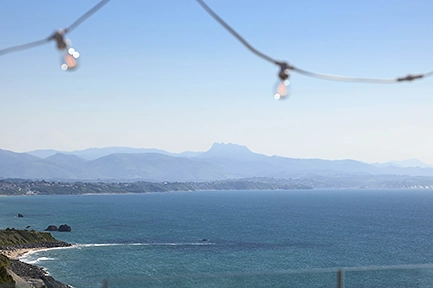 Vue panoramique sur la baie de Biarritz et les Pyrénées depuis un rooftop, avec une guirlande lumineuse en premier plan