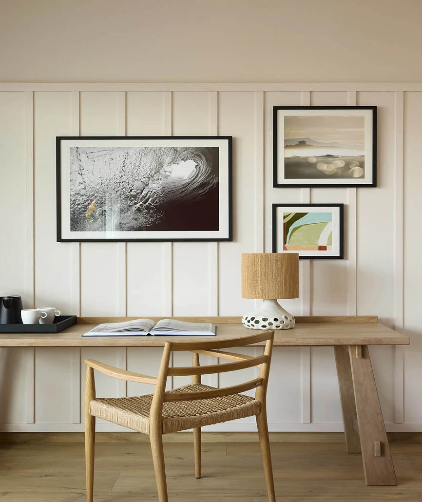 Bureau en chêne avec chaise tressée devant un mur lambrisé orné de trois œuvres encadrées à thème marin et naturel.