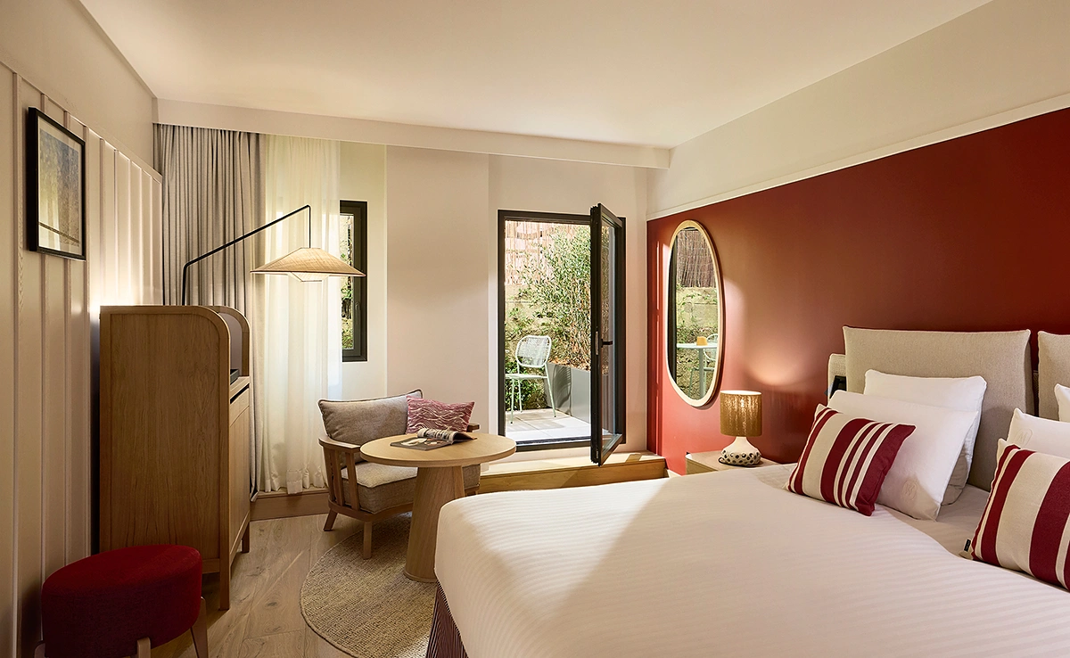 Chambre d'hôtel cosy avec grand lit, mur terracotta, miroir ovale doré et terrasse privée végétalisée