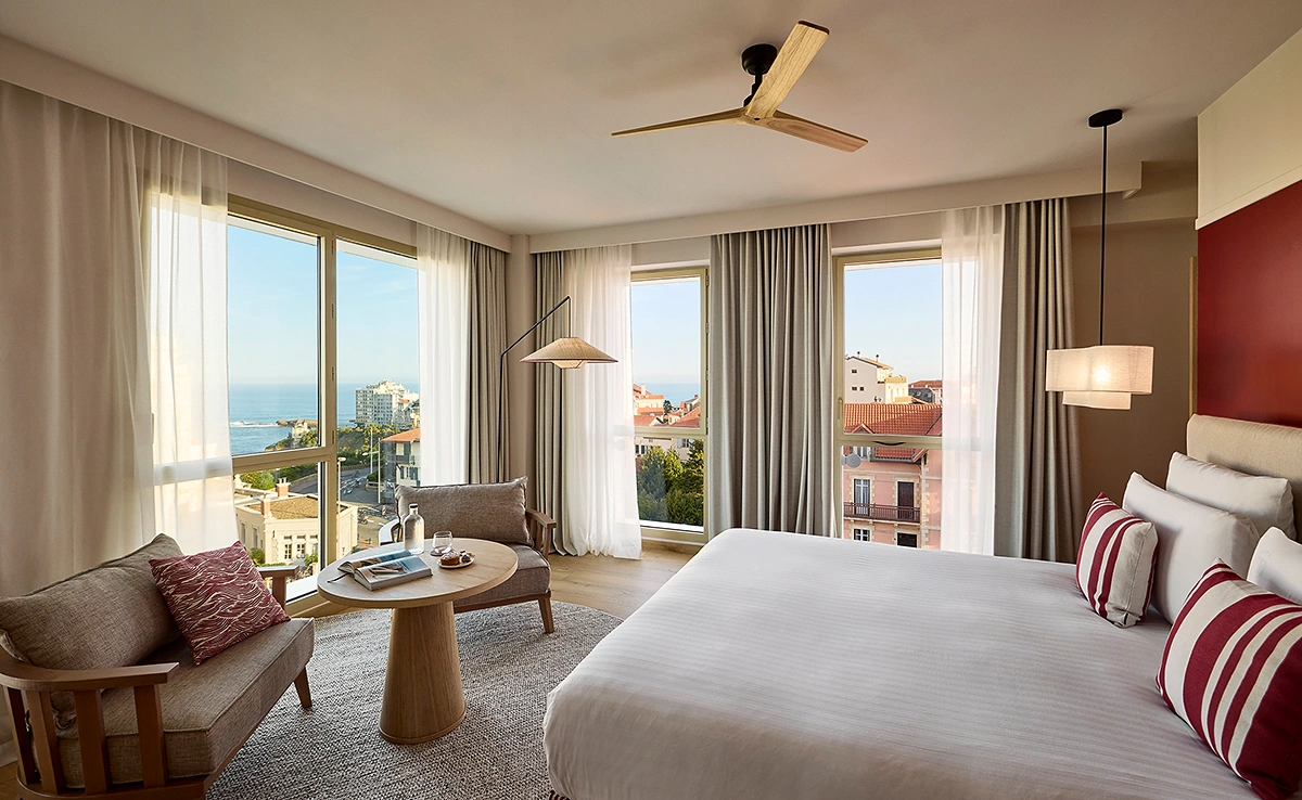 Chambre panoramique de l'hôtel Le Talaia Mgallery Biarritz avec lit king-size, ventilateur de plafond et vue sur la ville et l'océan