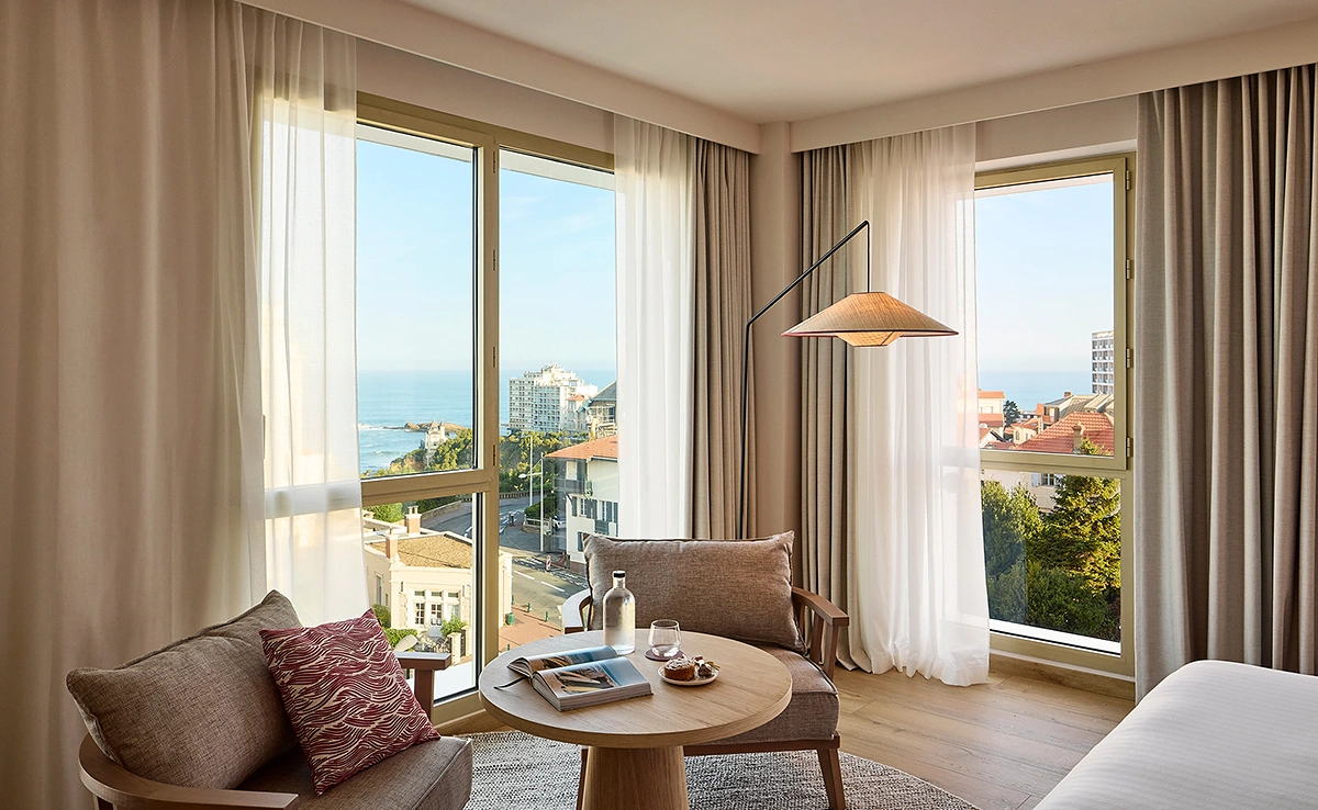 Chambre d'hôtel moderne avec vue sur la mer de Biarritz, décor chaleureux en tons beiges et bois naturel