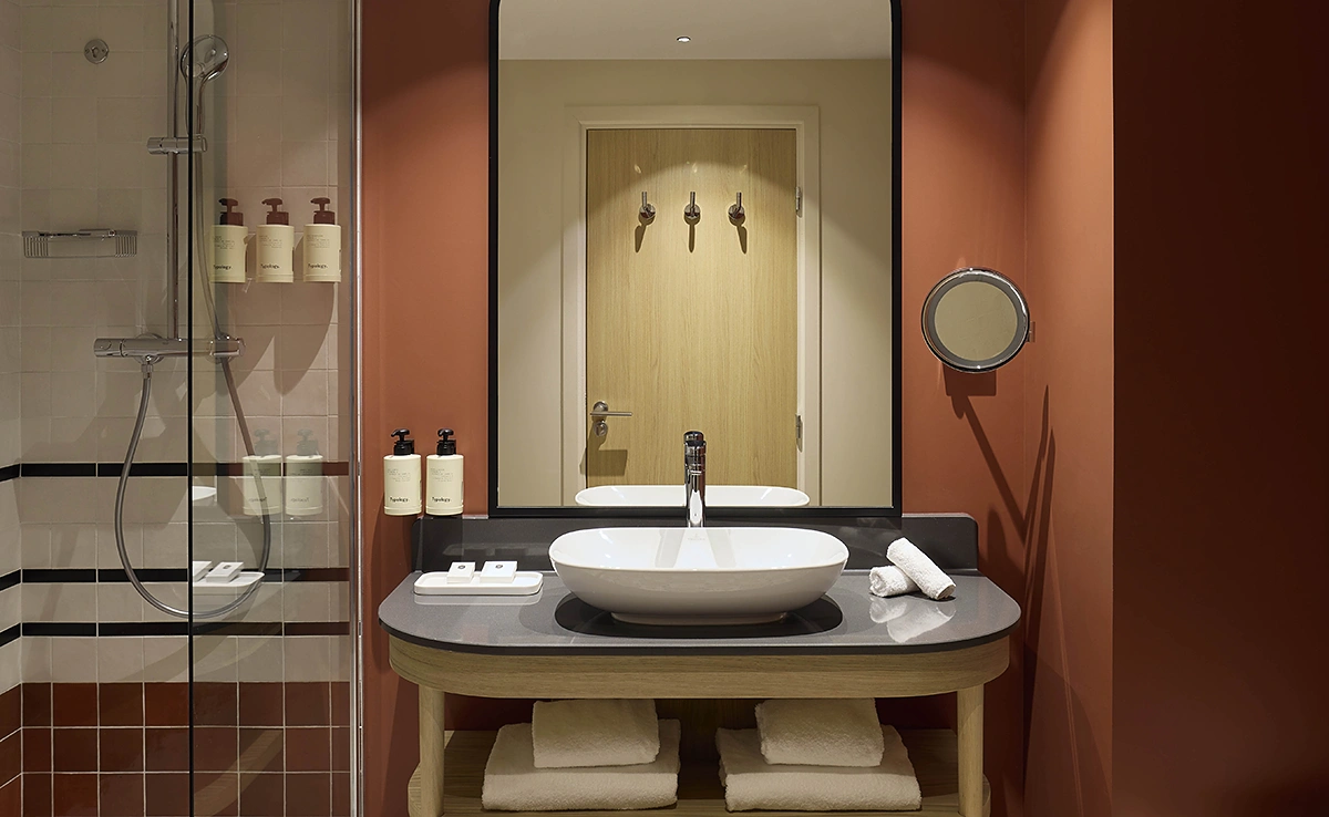 Salle de bain de l'hôtel Le Talaia Mgallery Biarritz avec vasque ronde, murs terracotta, douche à l'italienne et produits de soin Typology