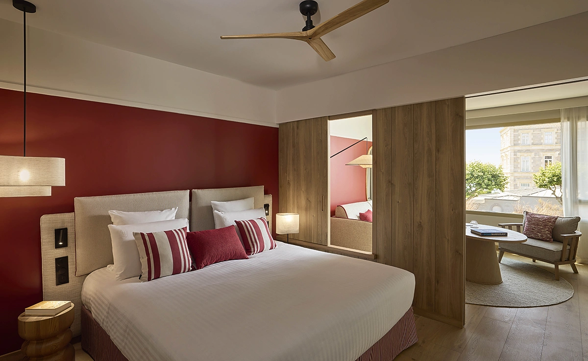 Chambre double de l'hôtel Le Talaia Mgallery Biarritz avec lit king-size, mur bordeaux, ventilateur de plafond et coin salon avec vue sur la ville
