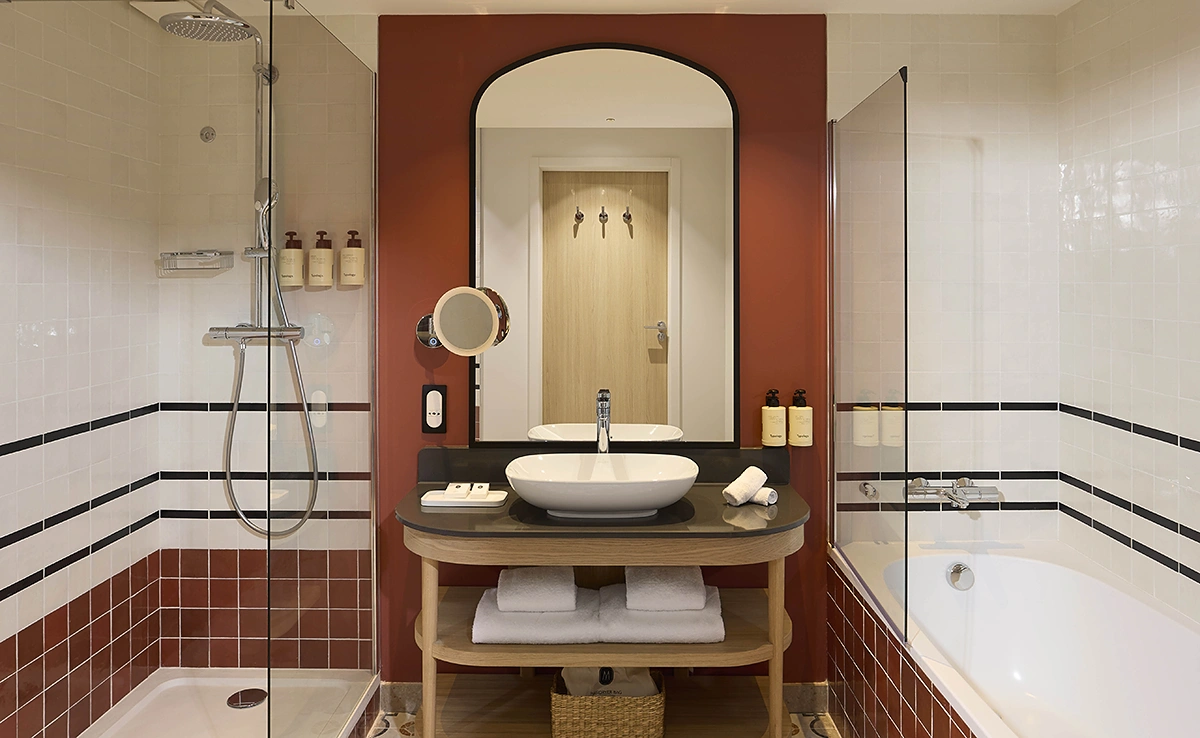 Salle de bain de l'hôtel Le Talaia Mgallery Biarritz avec vasque ronde, miroir cintré, carrelage terracotta, douche à l'italienne et baignoire