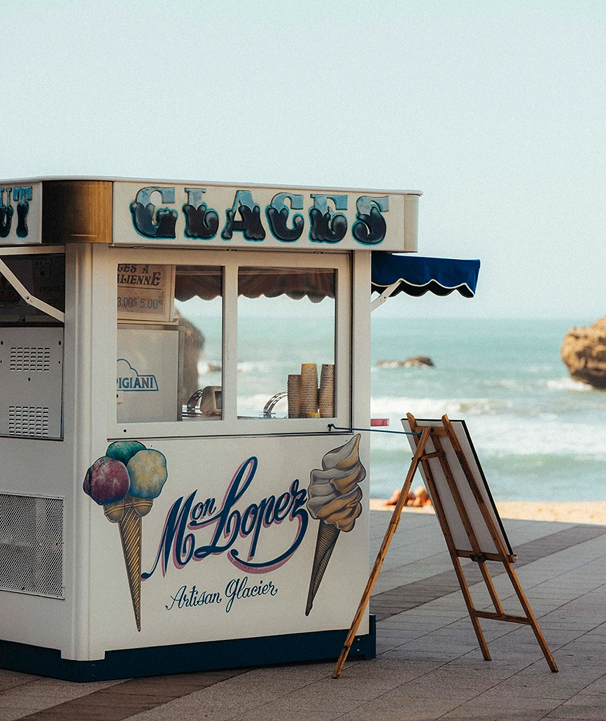 Kiosque à glaces artisanal "Mon Lopez" sur la promenade de Biarritz, avec l'océan et les rochers en arrière-plan.