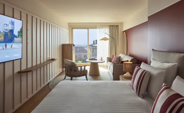 Chambre double de l'hôtel Le Talaia Mgallery Biarritz avec lit king-size, mur bordeaux, coin salon et vue sur la ville