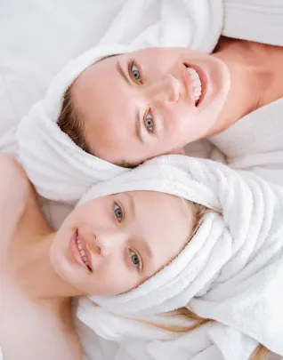 Deux femmes souriantes en peignoir et serviette blanche sur la tête, détendues après un soin au spa