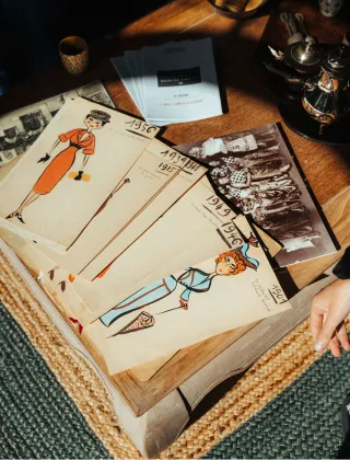 Collection de patrons de couture vintage des années 1950-1960 avec illustrations de mode féminines, accompagnés de photographies anciennes en noir et blanc, disposés sur une table en bois.
