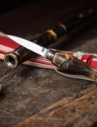 Couteau artisanal basque à manche en bois sculpté posé sur un tissu rayé rouge et blanc, photographié sur une surface en bois rustique dans une ambiance sombre et chaleureuse.
