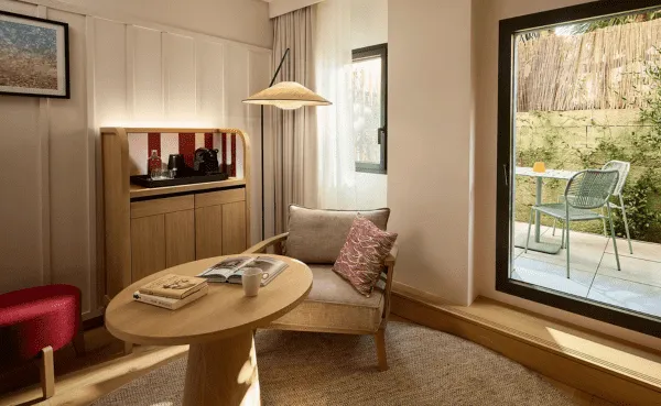 Coin salon de chambre d'hôtel avec fauteuil, table basse en bois et accès direct à une terrasse privée verdoyante