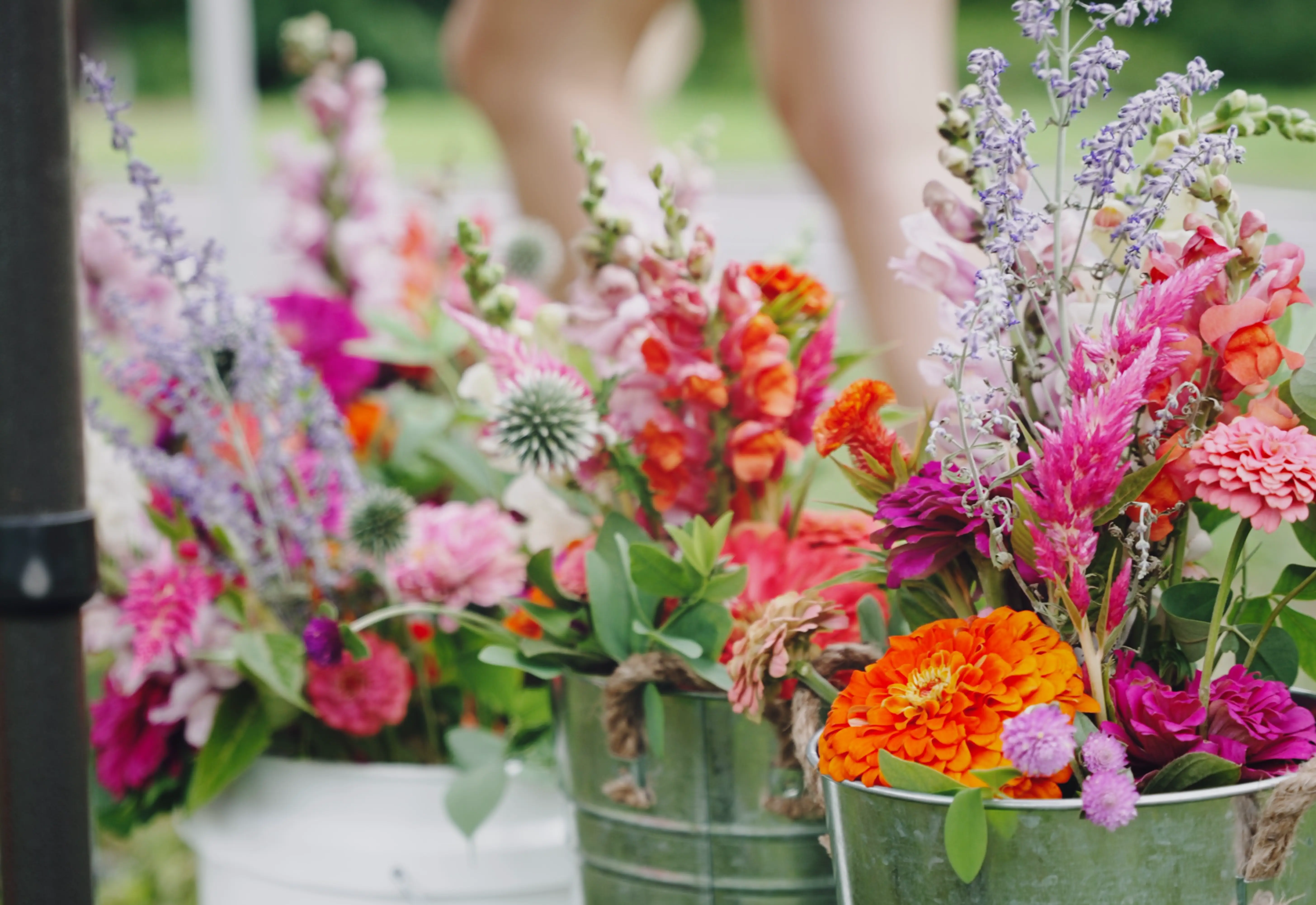Galvanized buckets filled with mixed summer bouquets — zinnias, snapdragons, celosia, and lavender — ready for pickup.