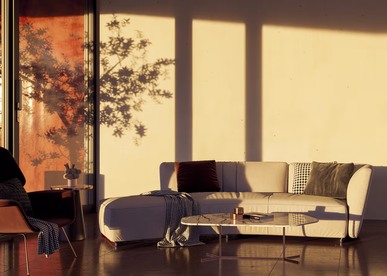 Sunlit modern living room with a cream-colored sectional sofa with pillows, a marble coffee table, and a chair casting shadows of a tree on the wall.