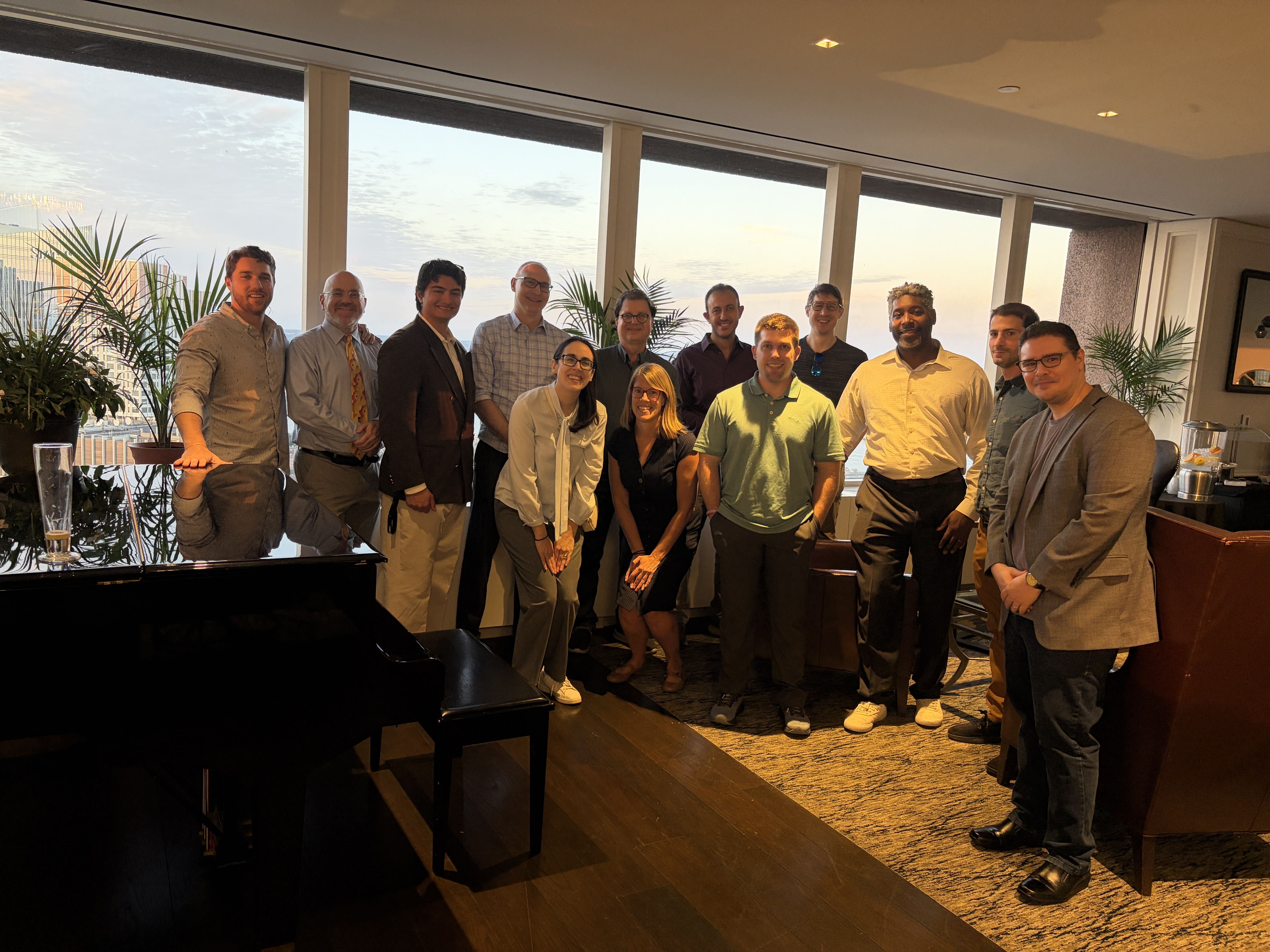 Alumni group photo beside the piano at the UMass Club, Boston, at sunset