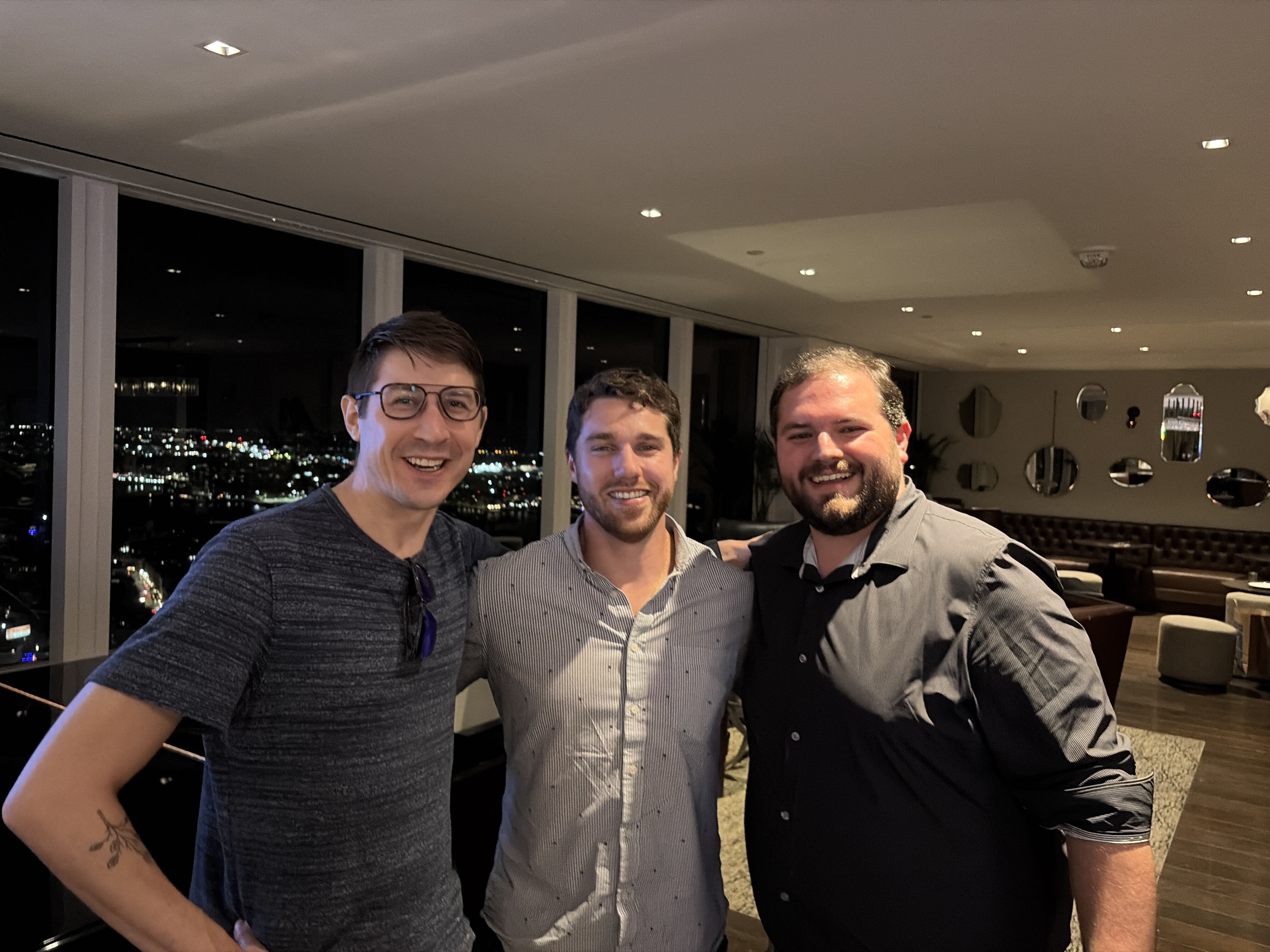 Three founders at the UMass Club after dark with Boston lit up behind them