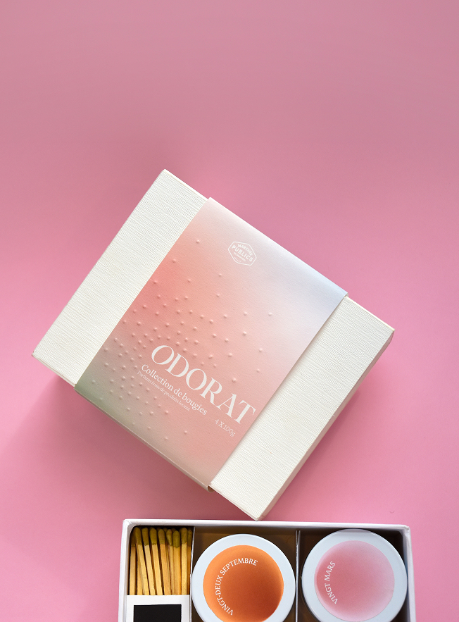 Open box containing two scented candles labeled with dates and a matchbox on a pink background. Credit: May-lee Abel