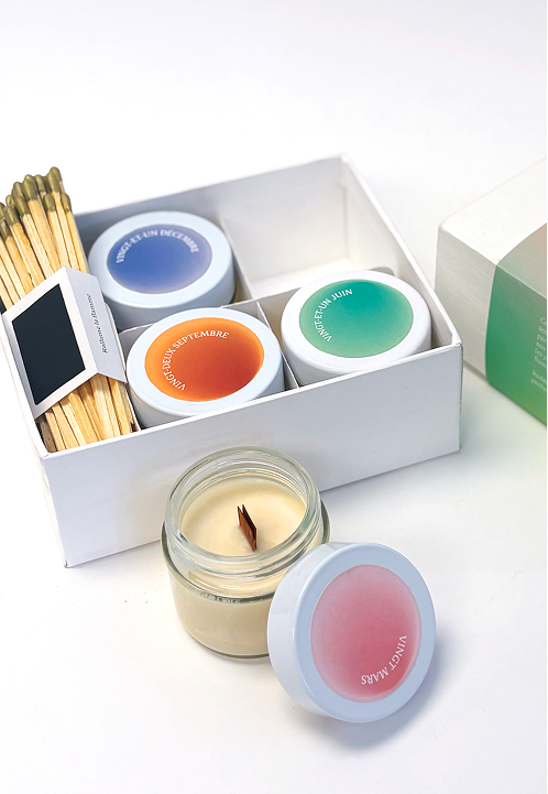Set of four scented candles in a white box with colorful round labels and a bundle of matches. Credit: May-lee Abel