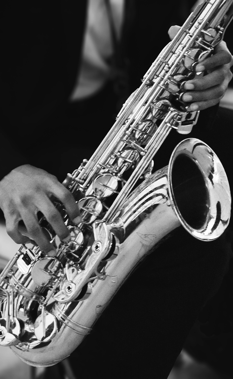 Close-up of a person playing a shiny saxophone with both hands in black and white. credit: Laura Riviera