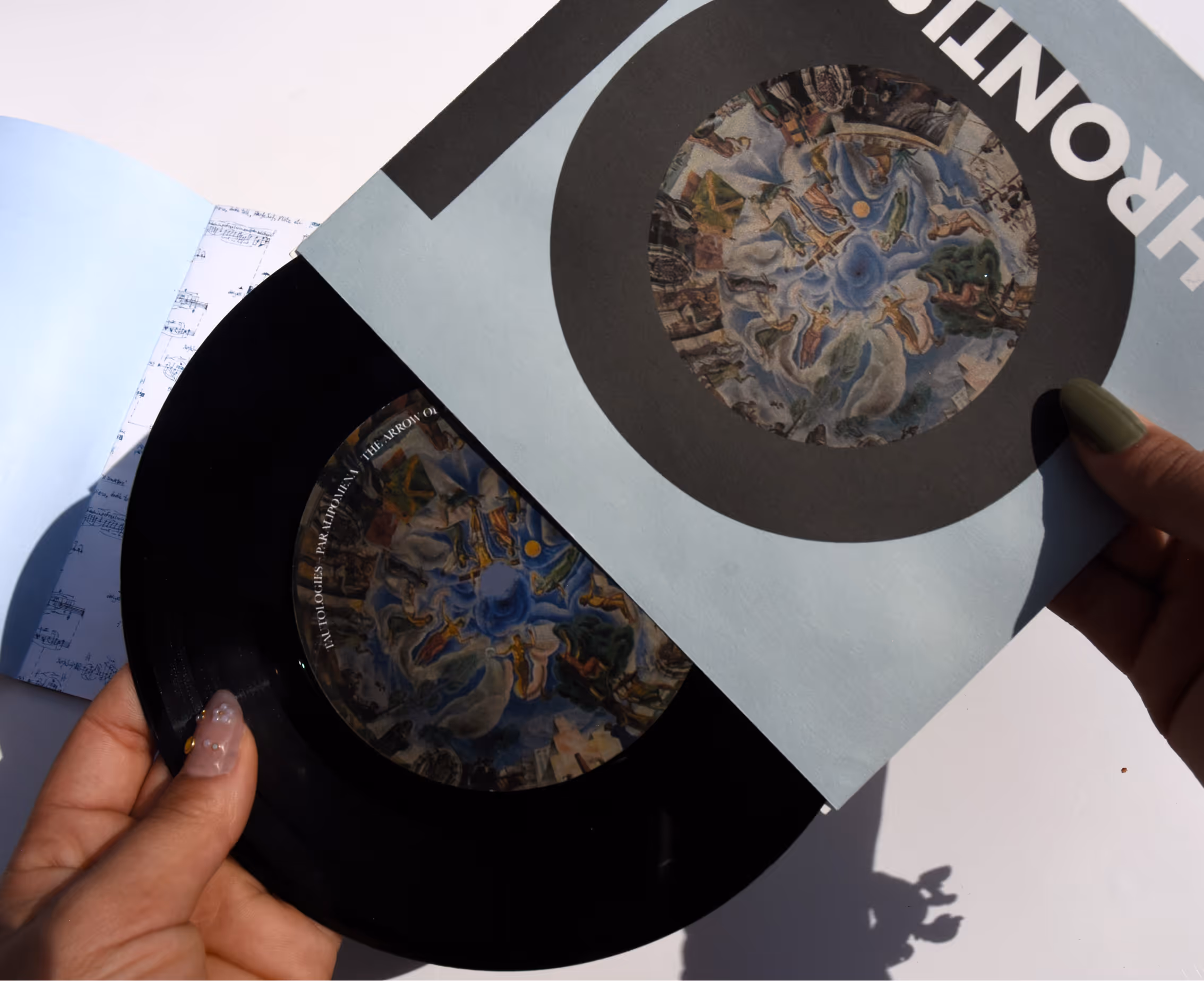 Hands holding a vinyl record and its cover with circular artwork of a painted sky and figures. Credit: May-Lee Abel